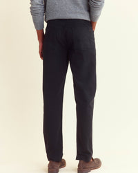 A person stands facing away, wearing a gray long-sleeve sweater, black pants, and brown shoes, against a plain light background.