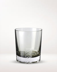 A clear glass tumbler with a thick base, featuring a decorative white diagonal stripe near the bottom, set against a plain light background.