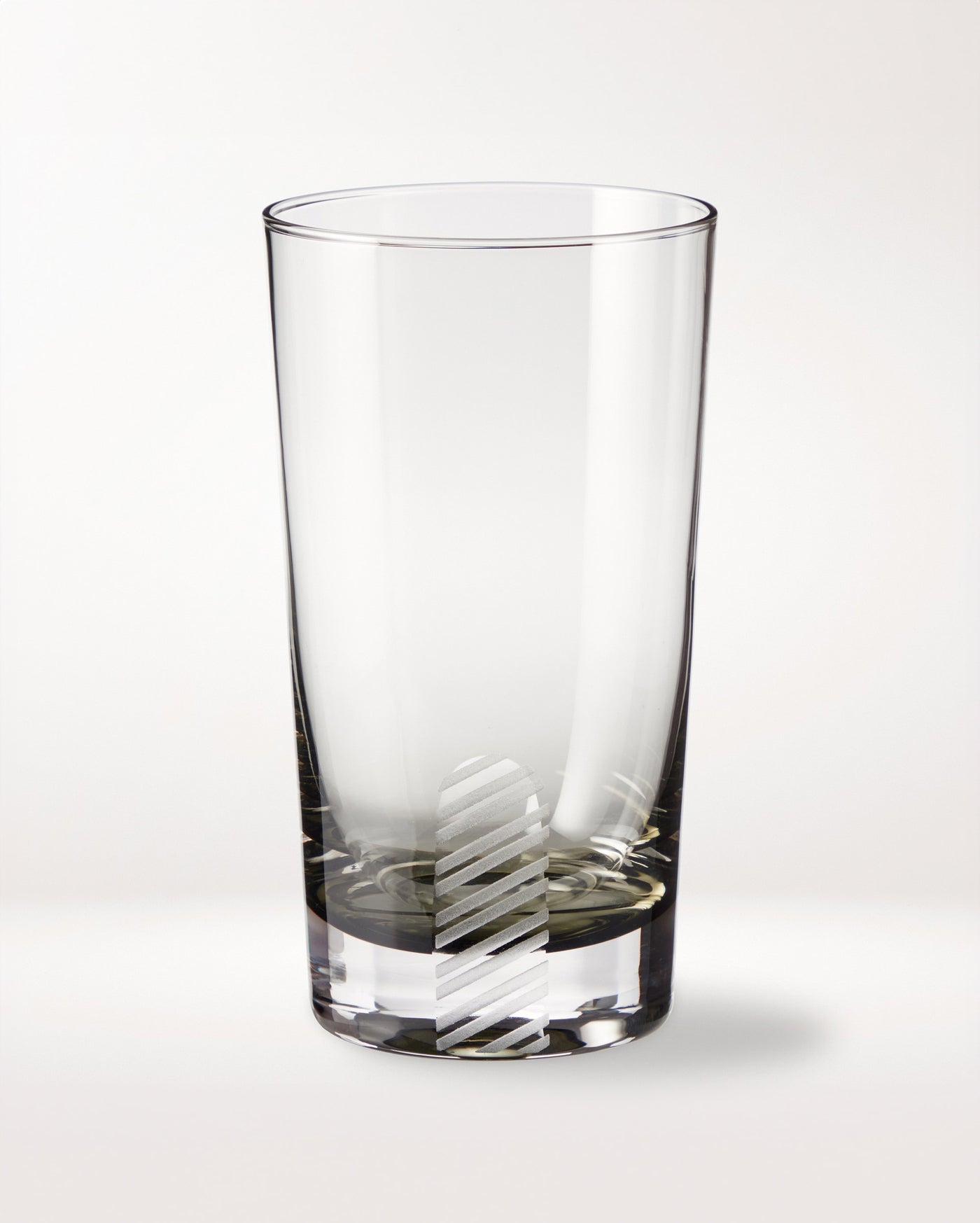 A clear empty glass tumbler with a vertical, diagonal-striped frosted pattern near the base, placed on a plain white background.
