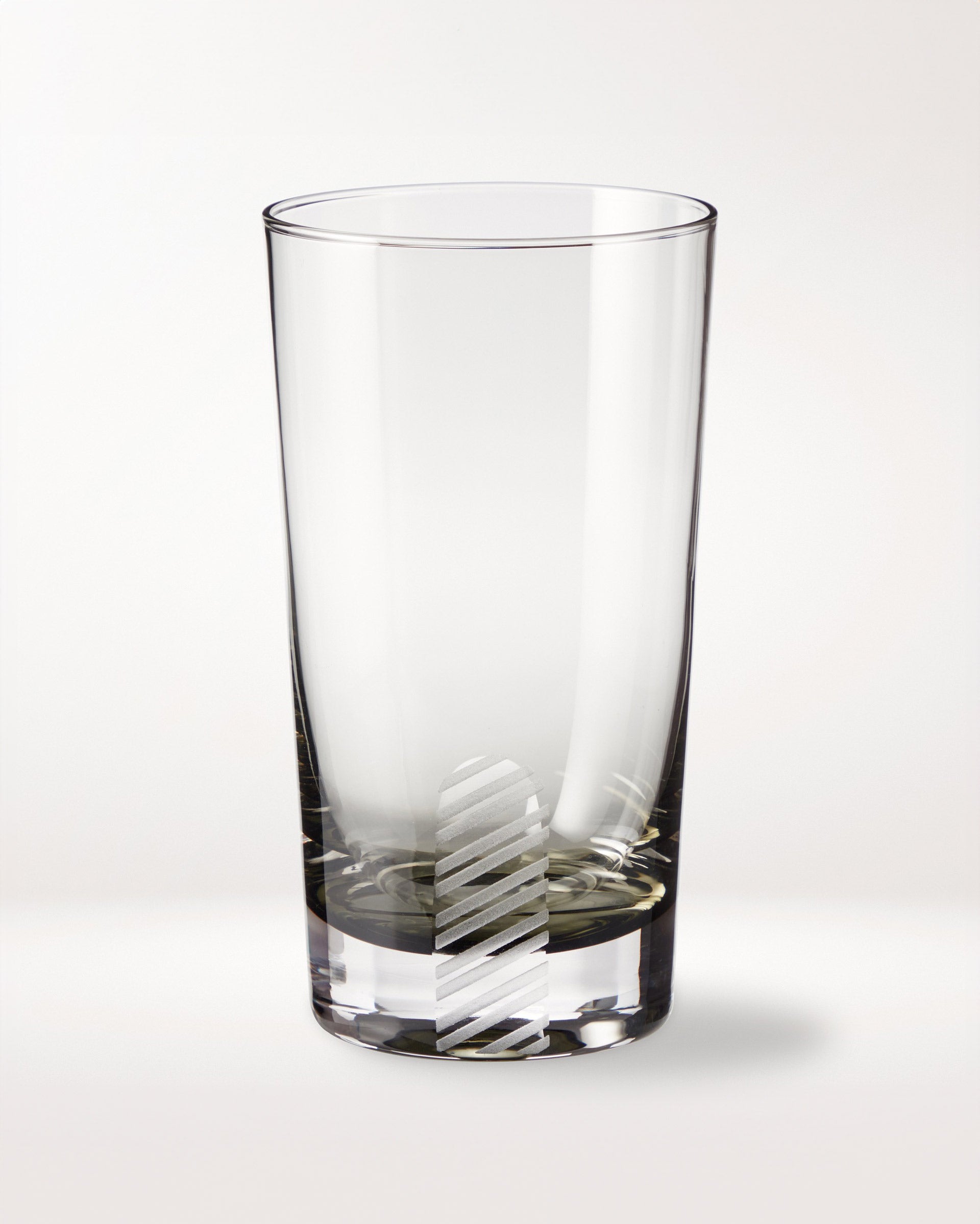 A clear empty glass tumbler with a vertical, diagonal-striped frosted pattern near the base, placed on a plain white background.