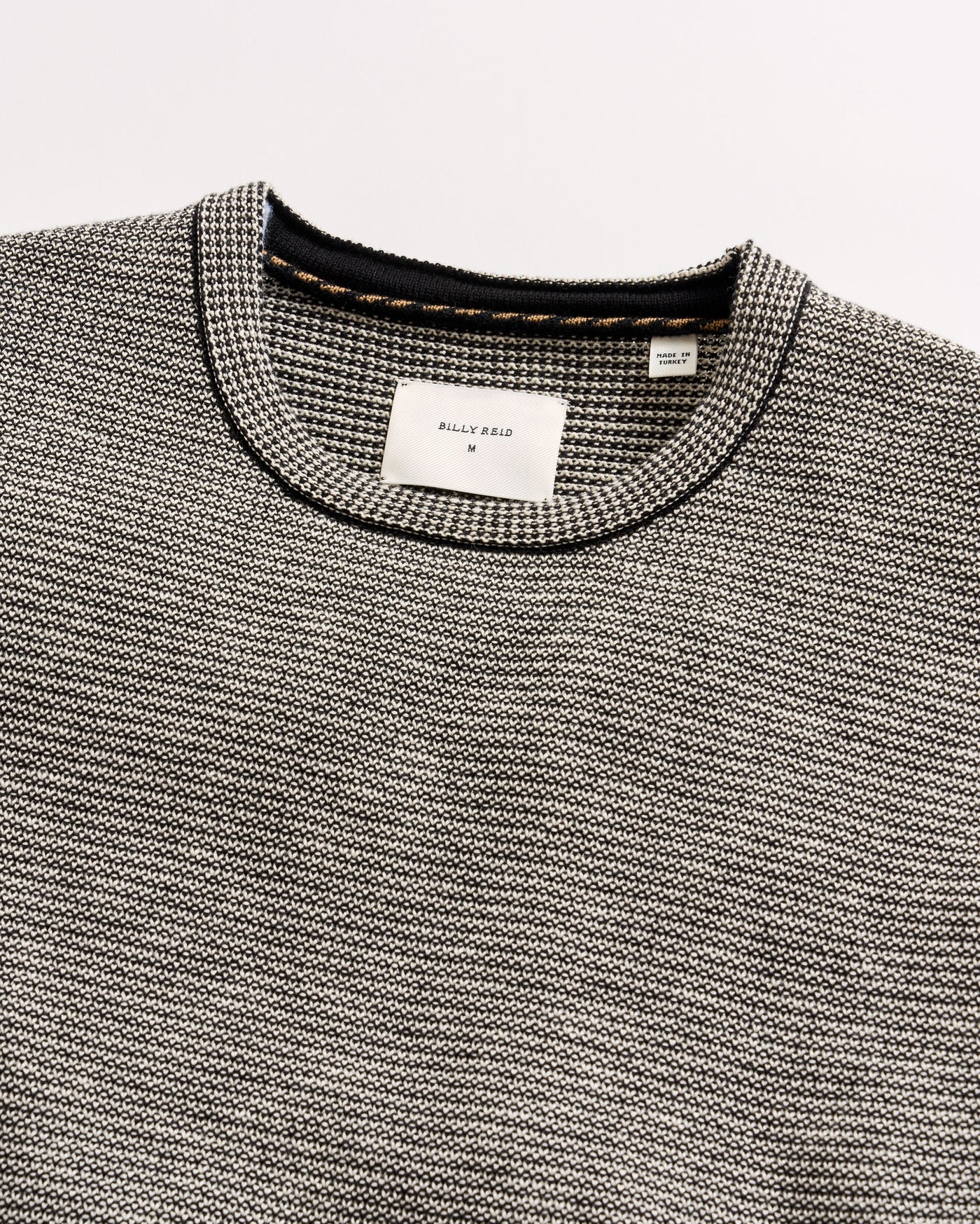 Close-up of a gray textured sweater with brand labels on a light gray background