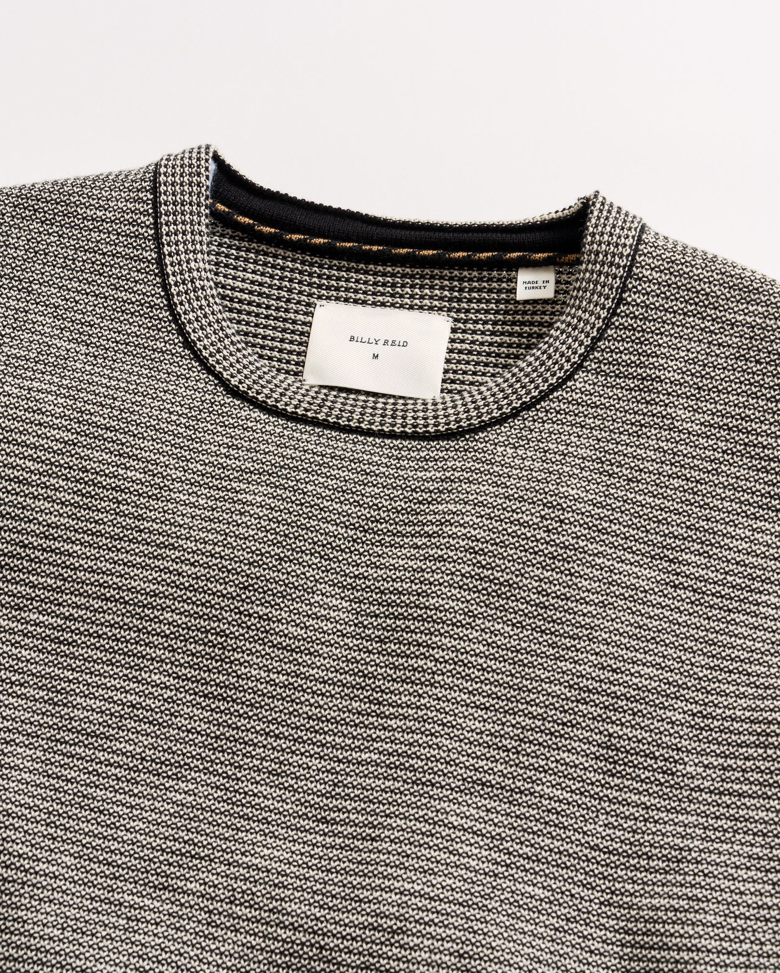 Close-up of a gray textured sweater with brand labels on a light gray background