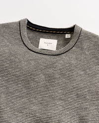 Close-up of a gray textured sweater with brand labels on a light gray background