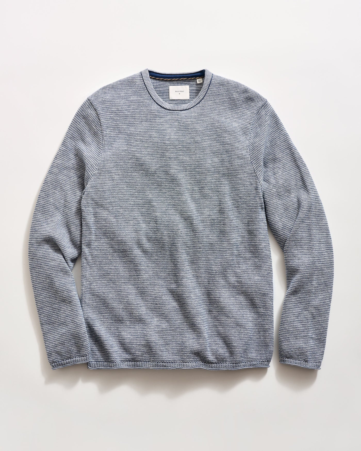 A blue striped long-sleeve crewneck knit sweater laid flat against a light off-white background.