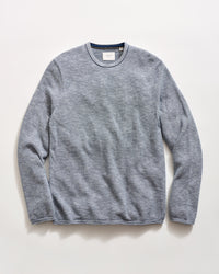 A blue striped long-sleeve crewneck knit sweater laid flat against a light off-white background.