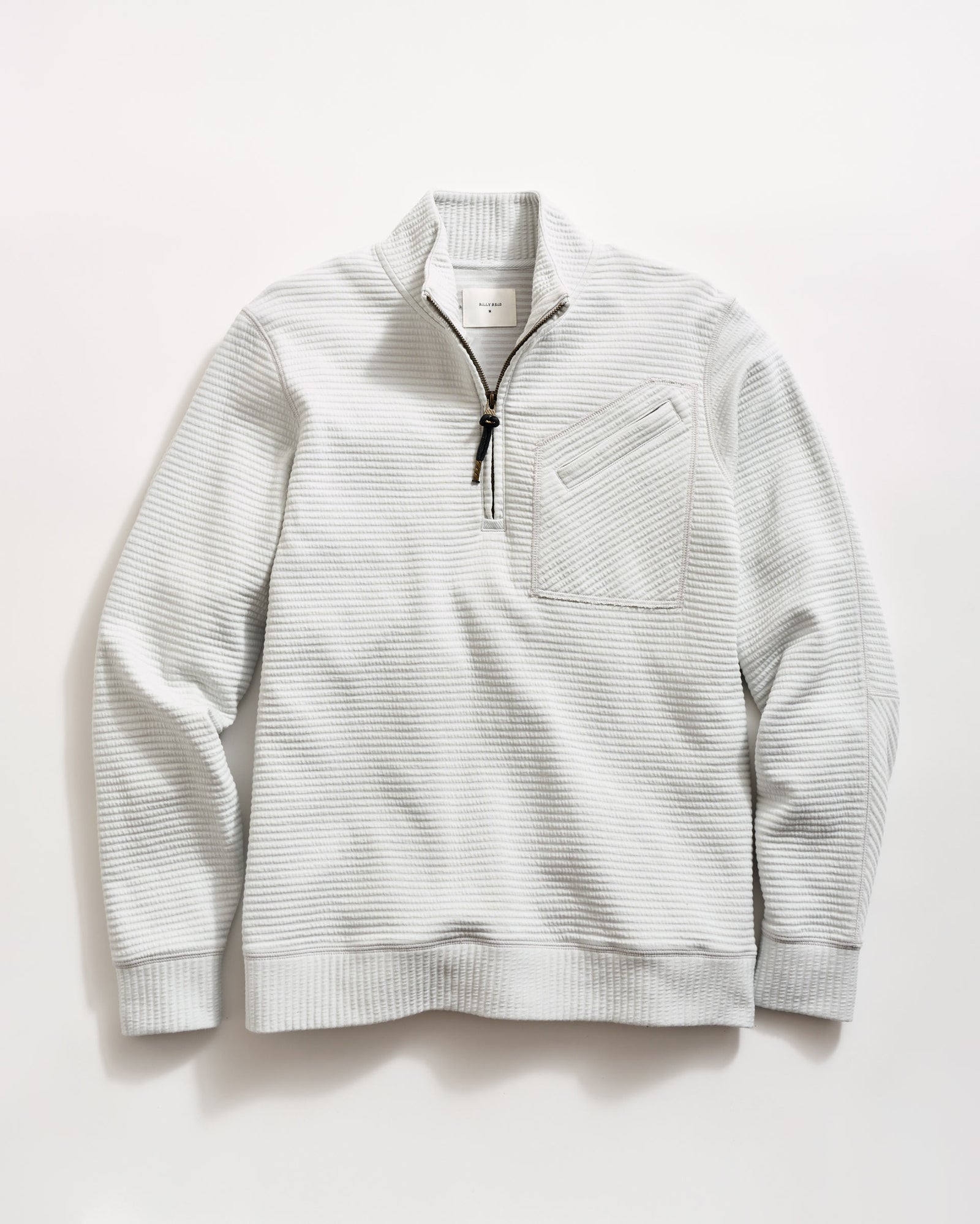 Light gray, long-sleeve pullover sweater with a quarter-zip front, black zipper pull, ribbed cuffs and hem, and a textured waffle pattern. A small chest pocket with a diagonal opening is on the left side.