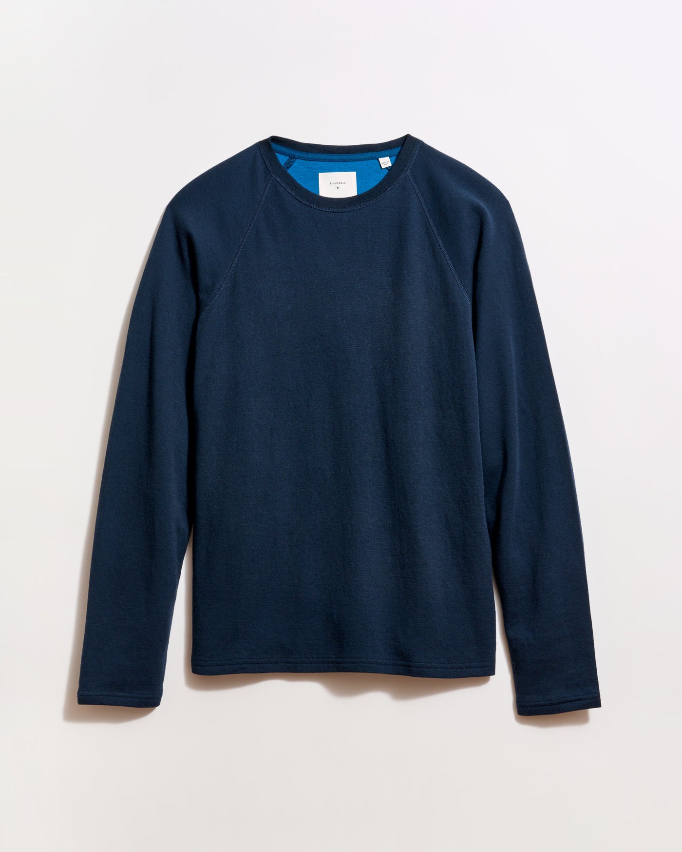 A plain, long-sleeved navy blue crewneck shirt is laid flat on a light background. The shirt has a simple design with no visible patterns or logos.