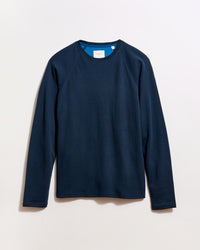 A plain, long-sleeved navy blue crewneck shirt is laid flat on a light background. The shirt has a simple design with no visible patterns or logos.