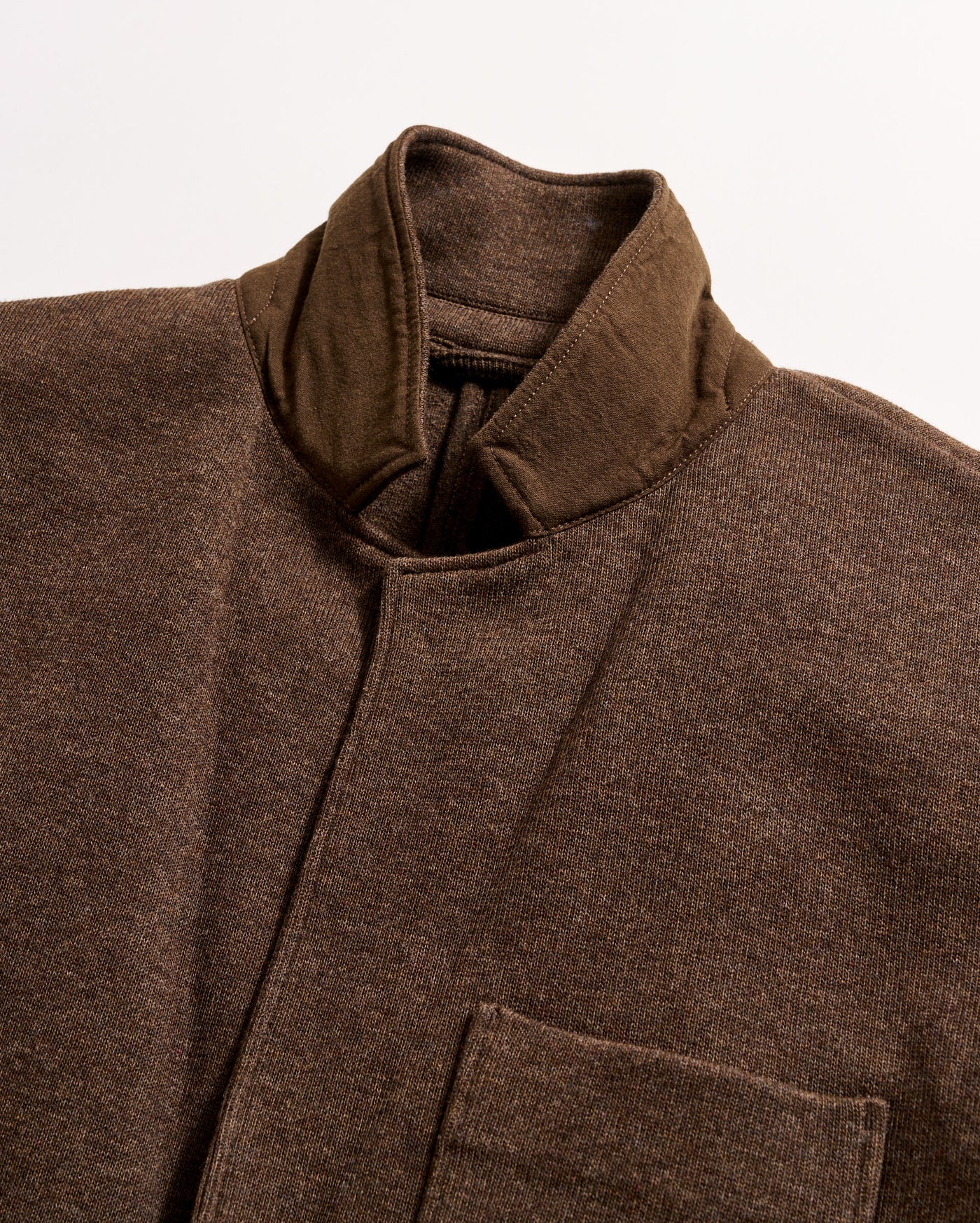 A close-up of a brown jacket with a stand-up collar and a visible chest pocket, made from a textured fabric, shown against a plain white background.