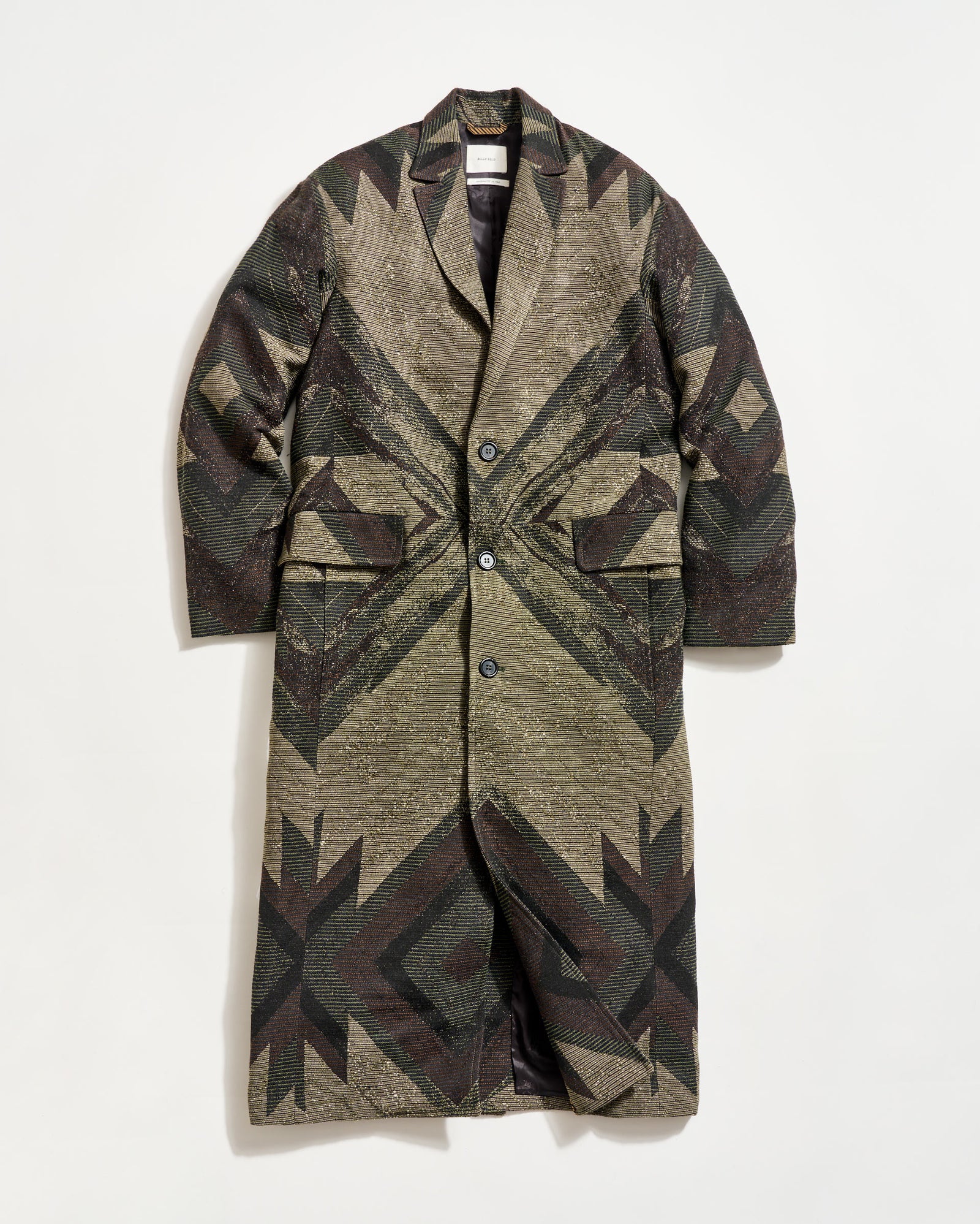 A long, patterned overcoat with a geometric design in earthy tones, featuring a notched collar, button closure, and two large front flap pockets, displayed against a plain white background.