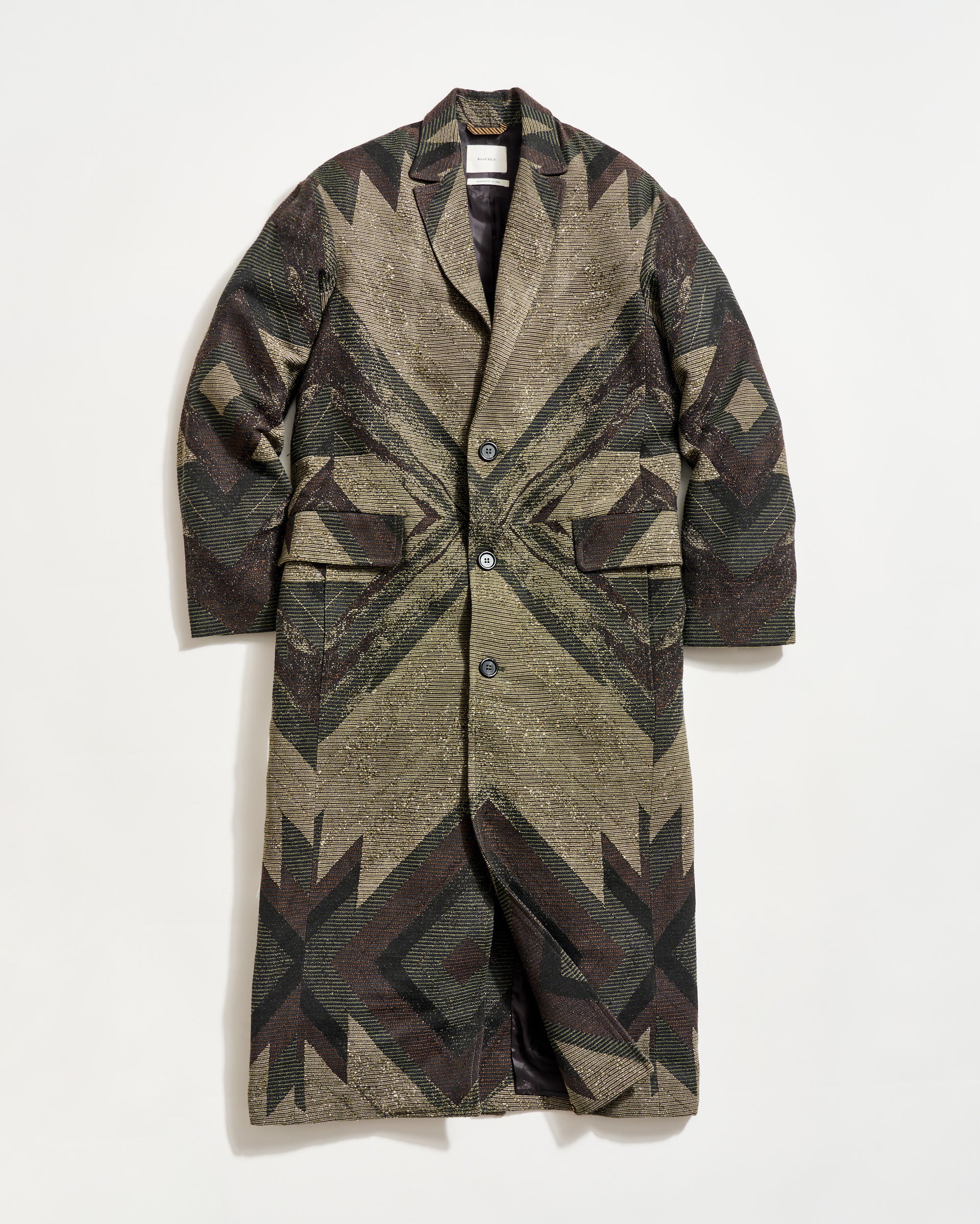 A long, patterned overcoat with a geometric design in earthy tones, featuring a notched collar, button closure, and two large front flap pockets, displayed against a plain white background.