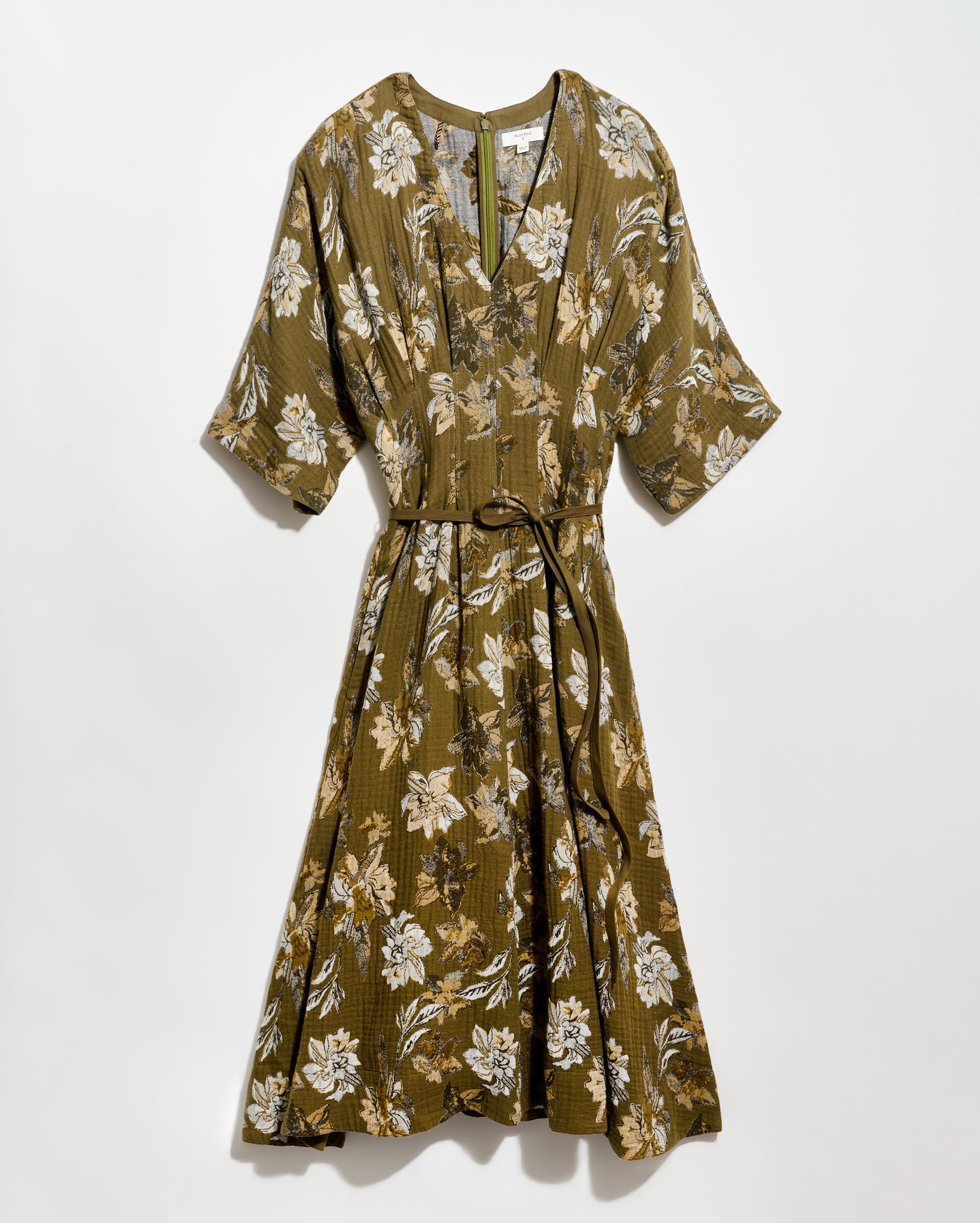 Olive green, knee-length dress with a white and tan floral pattern, short wide sleeves, a V-neckline, and a thin matching belt tied at the waist. The dress is displayed against a plain white background.