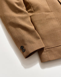 A close-up of a brown textured blazer sleeve with two black buttons on the cuff, shown on a light background. The blazer features a large front pocket.