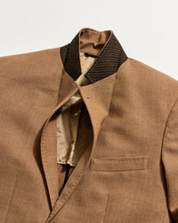 A close-up of a brown suit jacket with a standing collar and a black-striped inner collar. The jacket is partially open, revealing a beige lining with a subtle pattern.