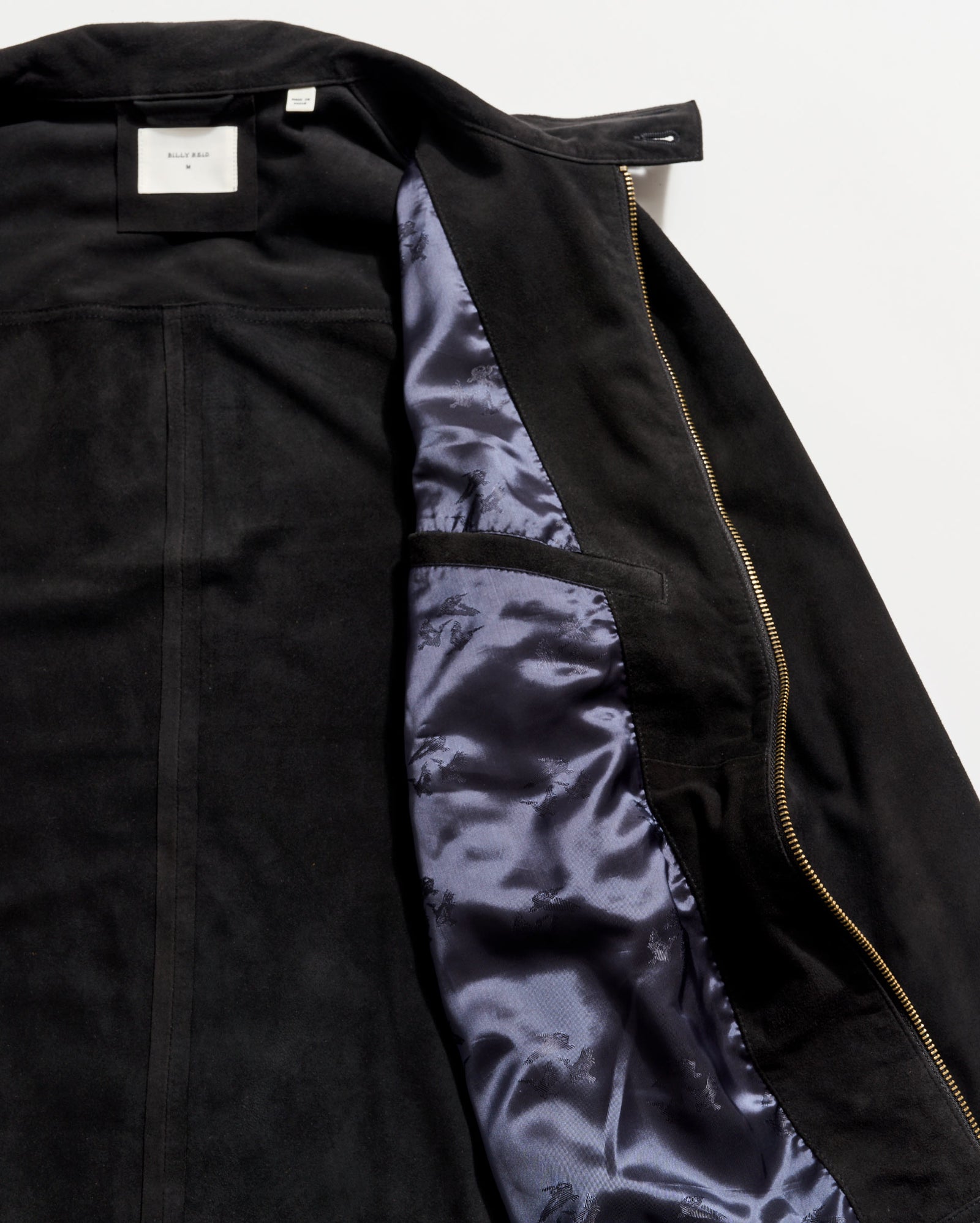Black suede jacket partially unzipped to reveal a shiny dark blue satin lining and an interior pocket on the left side, with a white label visible at the collar.