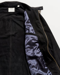 Black suede jacket partially unzipped to reveal a shiny dark blue satin lining and an interior pocket on the left side, with a white label visible at the collar.