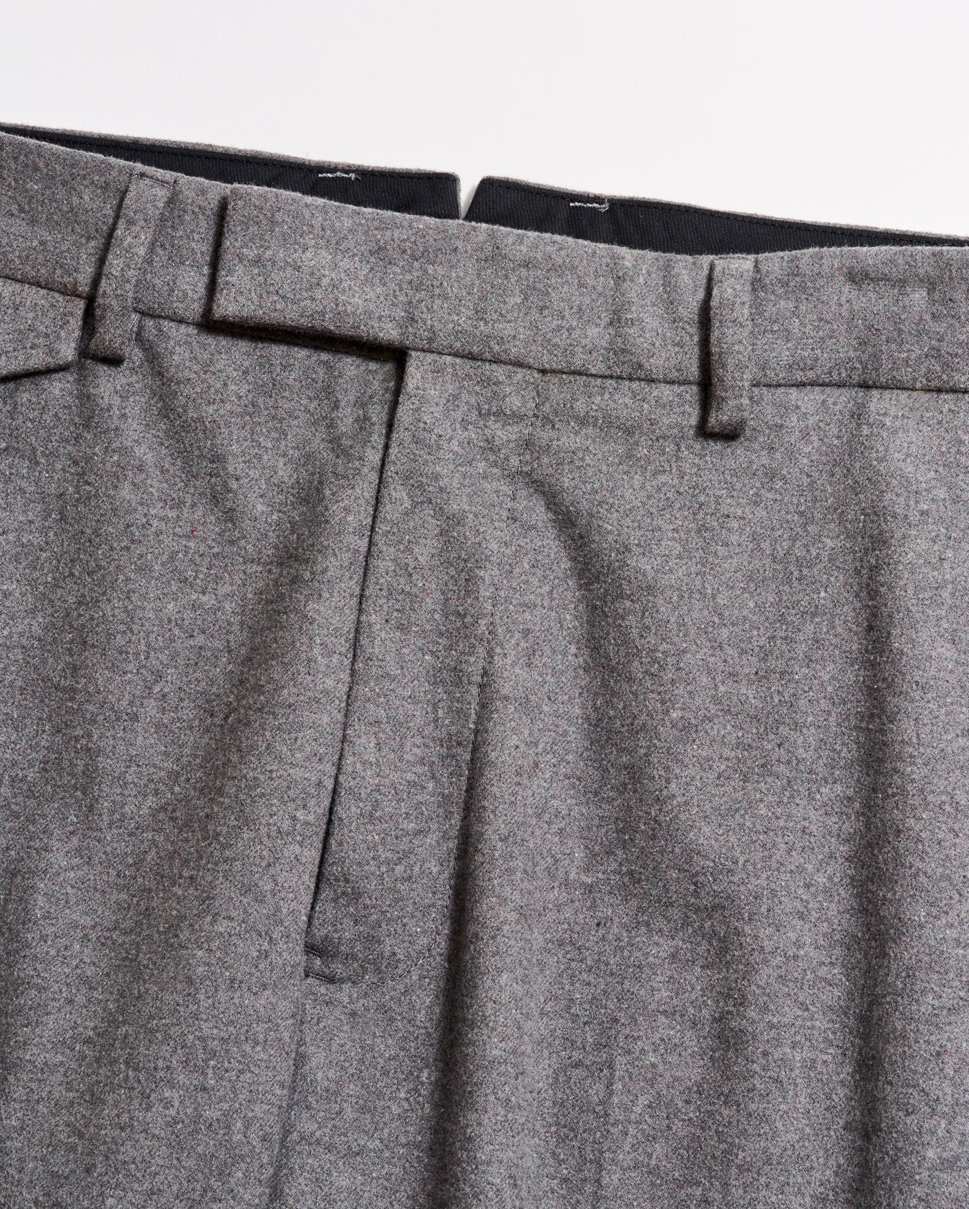 Close-up of the waistband and upper section of a pair of grey dress trousers, showing belt loops, pleats, and part of the zipper area against a plain background.