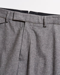 Close-up of the waistband and upper section of a pair of grey dress trousers, showing belt loops, pleats, and part of the zipper area against a plain background.