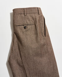 A pair of brown dress pants with a single back pocket featuring a button closure, shown neatly folded on a white background.