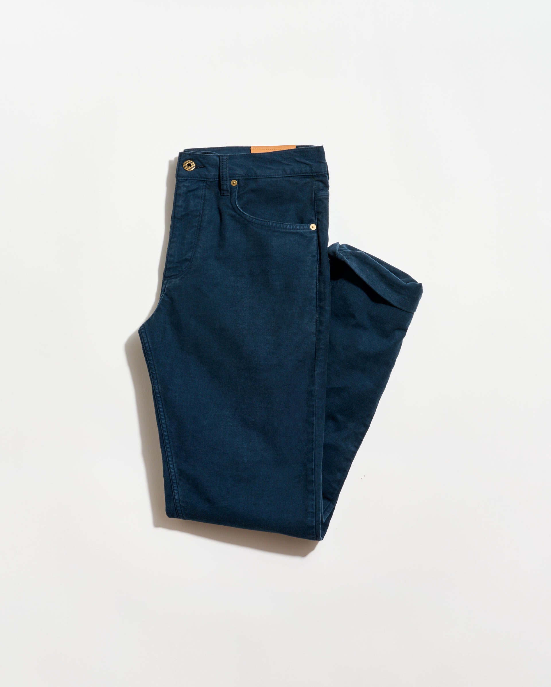 A pair of neatly folded dark blue jeans with visible front pockets and a brown leather patch on the waistband, displayed on a plain white background.