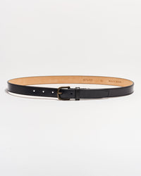 A black leather belt with a matte silver buckle is laid flat on a white background. The belt interior is tan, and size and brand details are stamped on the inside.
