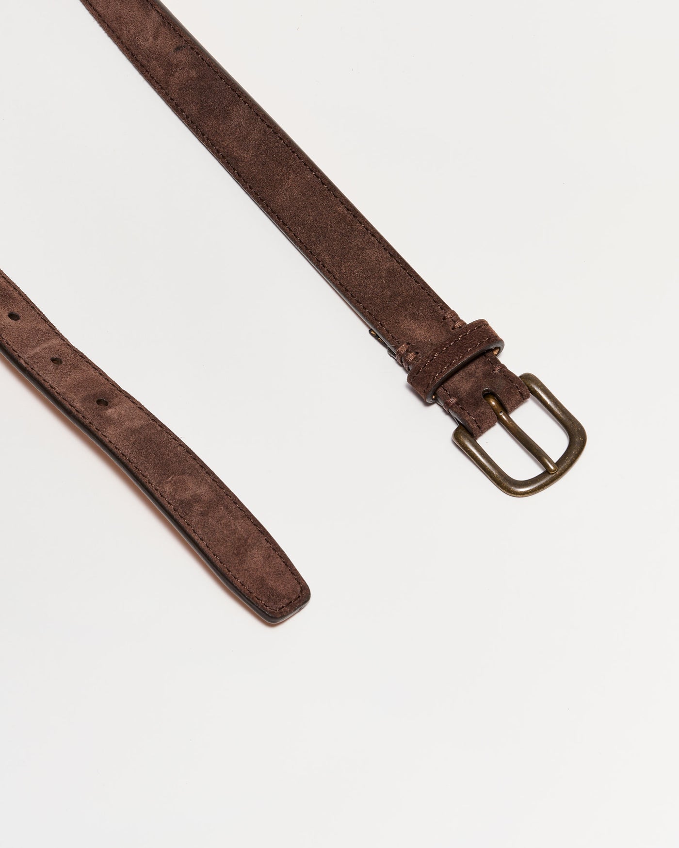 A brown suede belt with a brass buckle is laid flat on a white background. The belt is partially unbuckled, showing the pointed end and adjustment holes.
