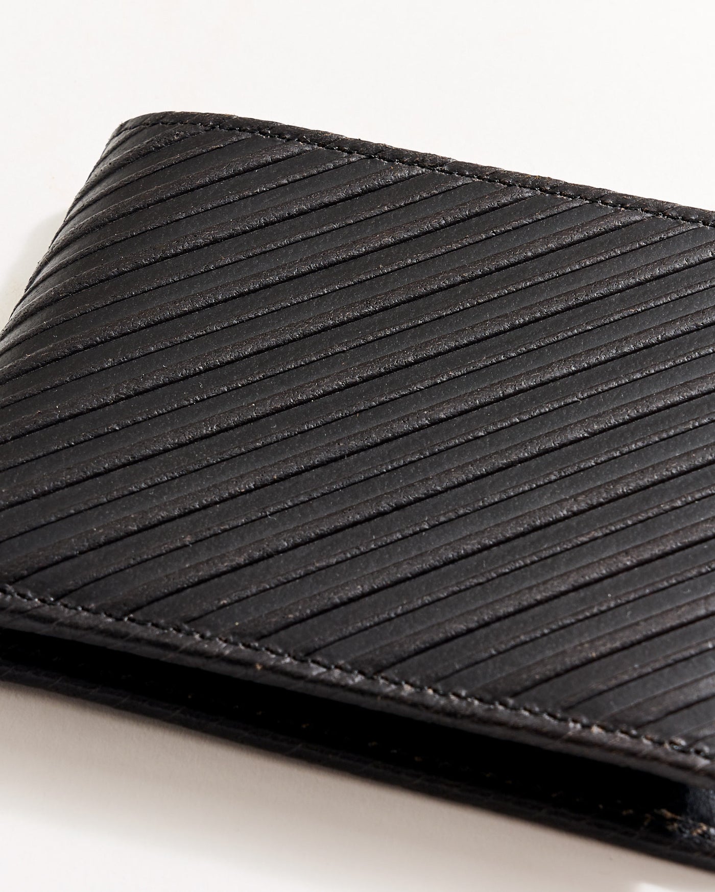 A close-up of a black leather wallet with diagonal textured lines, partially visible against a white background.