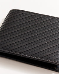 A close-up of a black leather wallet with diagonal textured lines, partially visible against a white background.