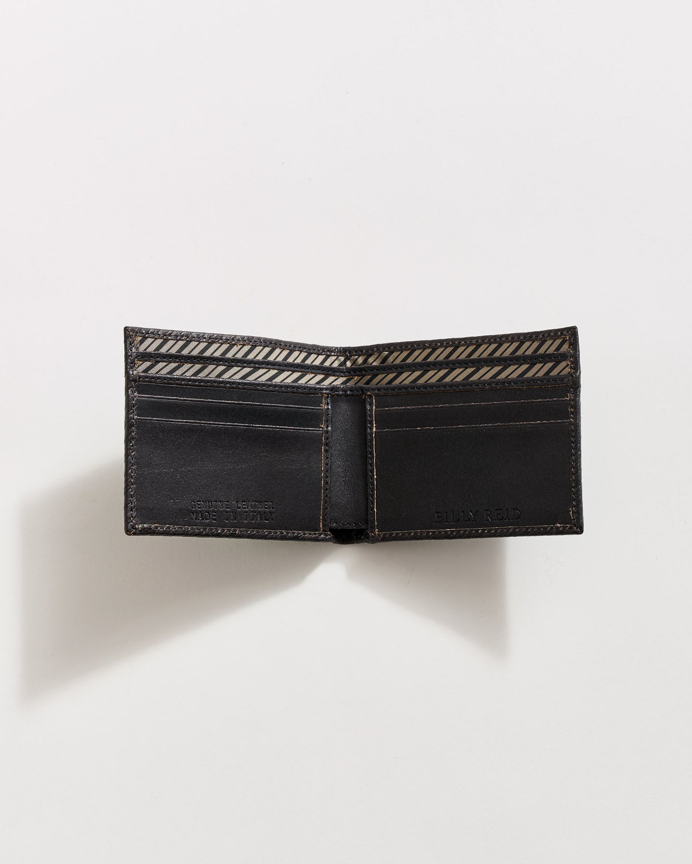 A black leather wallet is open on a white surface, showing multiple card slots and a patterned fabric lining inside the bill compartment. The wallet casts a soft shadow to the left.