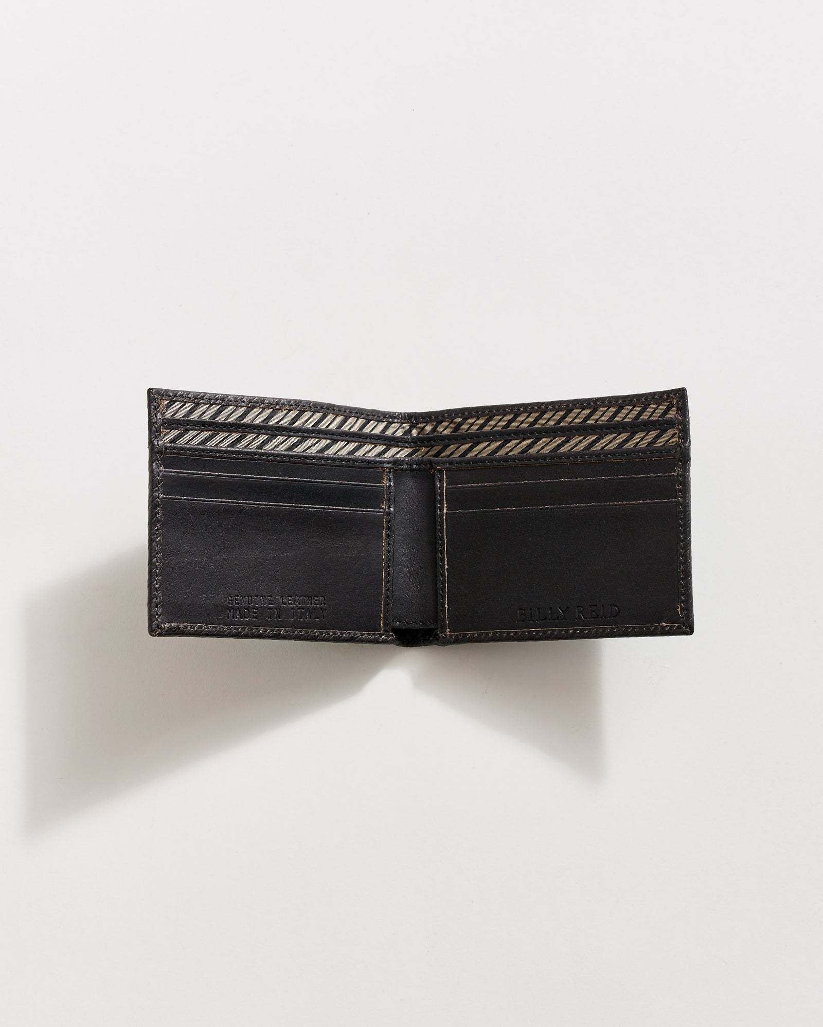 A black leather wallet is open on a white surface, showing multiple card slots and a patterned fabric lining inside the bill compartment. The wallet casts a soft shadow to the left.