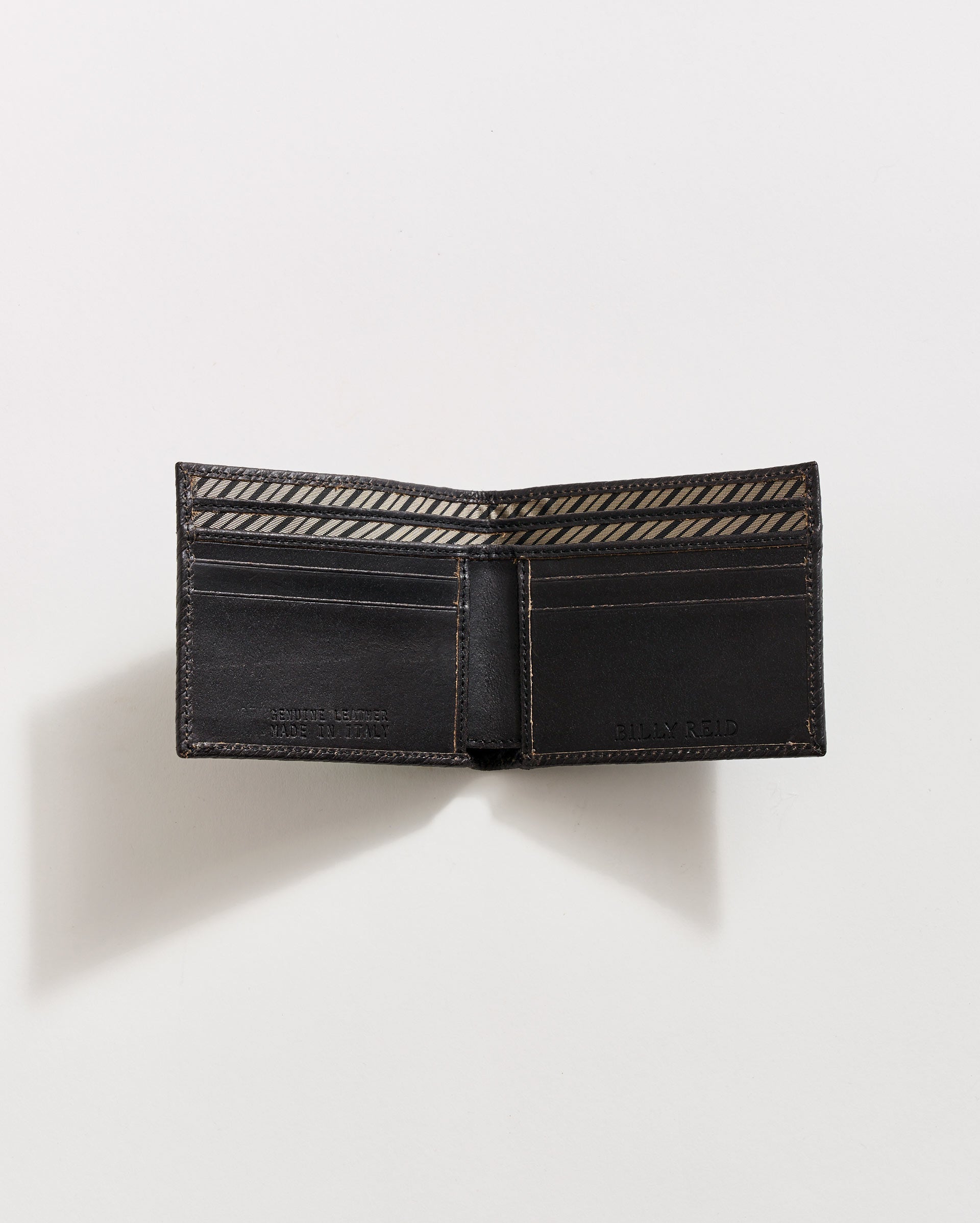 A black leather wallet is open on a white surface, showing multiple card slots and a patterned fabric lining inside the bill compartment. The wallet casts a soft shadow to the left.