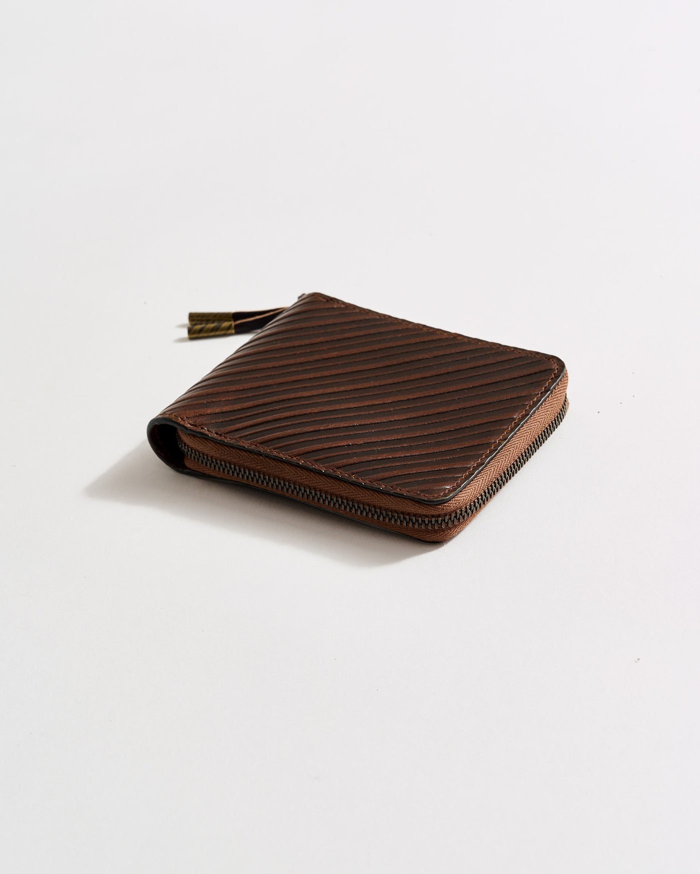 A brown leather zippered wallet with a textured diagonal line pattern is placed on a plain white surface.