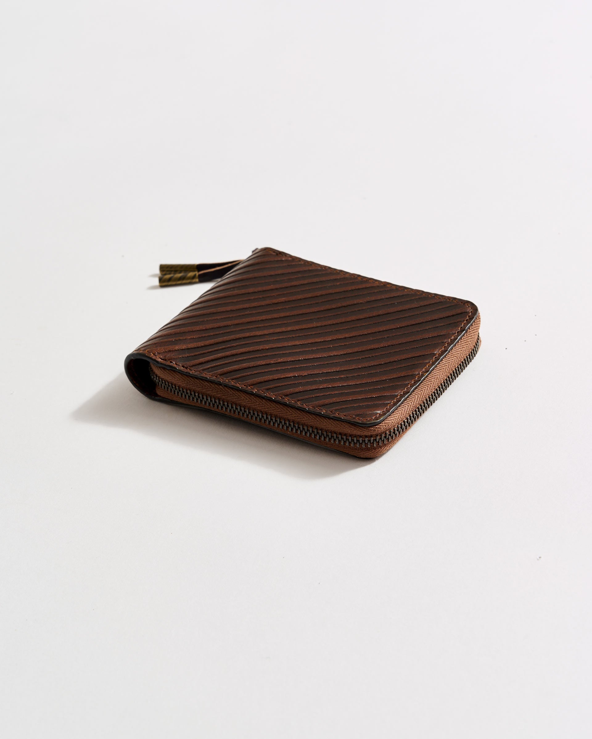 A brown leather zippered wallet with a textured diagonal line pattern is placed on a plain white surface.