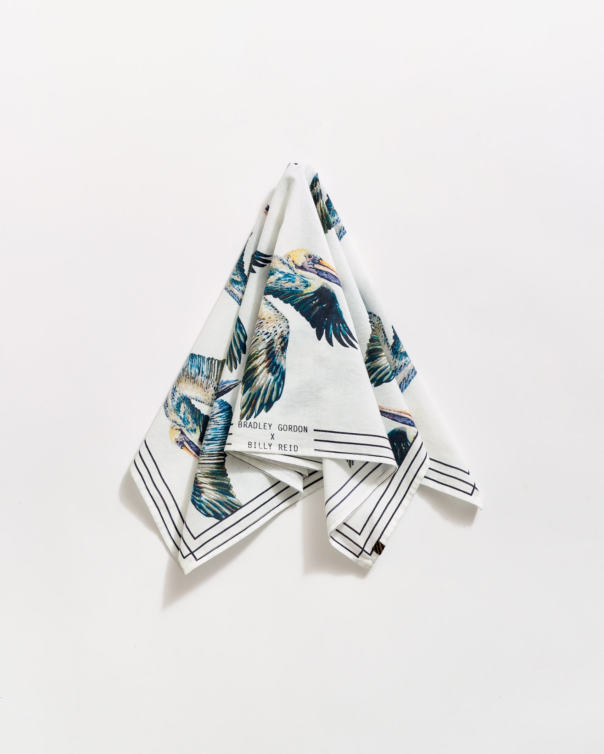 A folded white handkerchief hangs against a white background, featuring colorful bird illustrations and black border lines. The text Bradley Gordon and Billy Reid is visible near one corner.