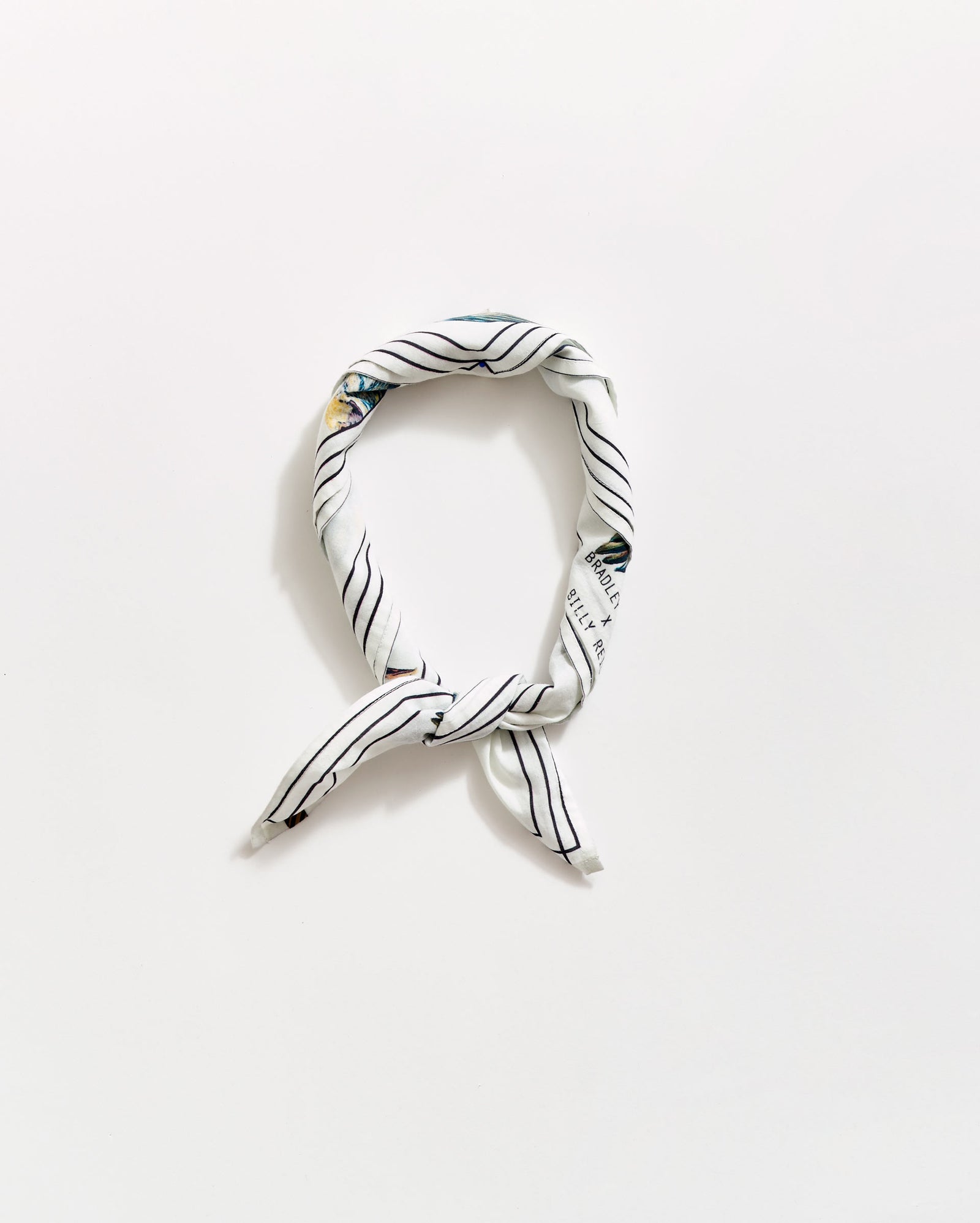 A white scarf with thin black diagonal stripes, tied in a loose knot and arranged in an oval shape on a plain white background.
