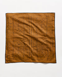 A brown square cloth with a black geometric and linear tribal pattern, bordered by a thin black edge, laid flat on a white background.