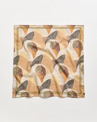 A square cloth napkin with an abstract, geometric pattern in earthy tones of beige, brown, rust, and olive green, featuring curved lines and shapes on a white background. The napkin is slightly wrinkled.