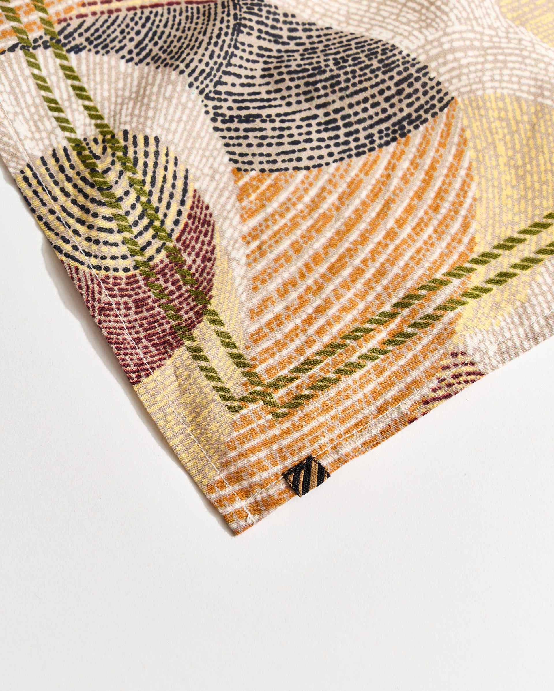 A close-up of a fabric corner with a colorful, abstract geometric pattern in orange, yellow, red, green, black, and white, featuring intersecting curved and straight lines.