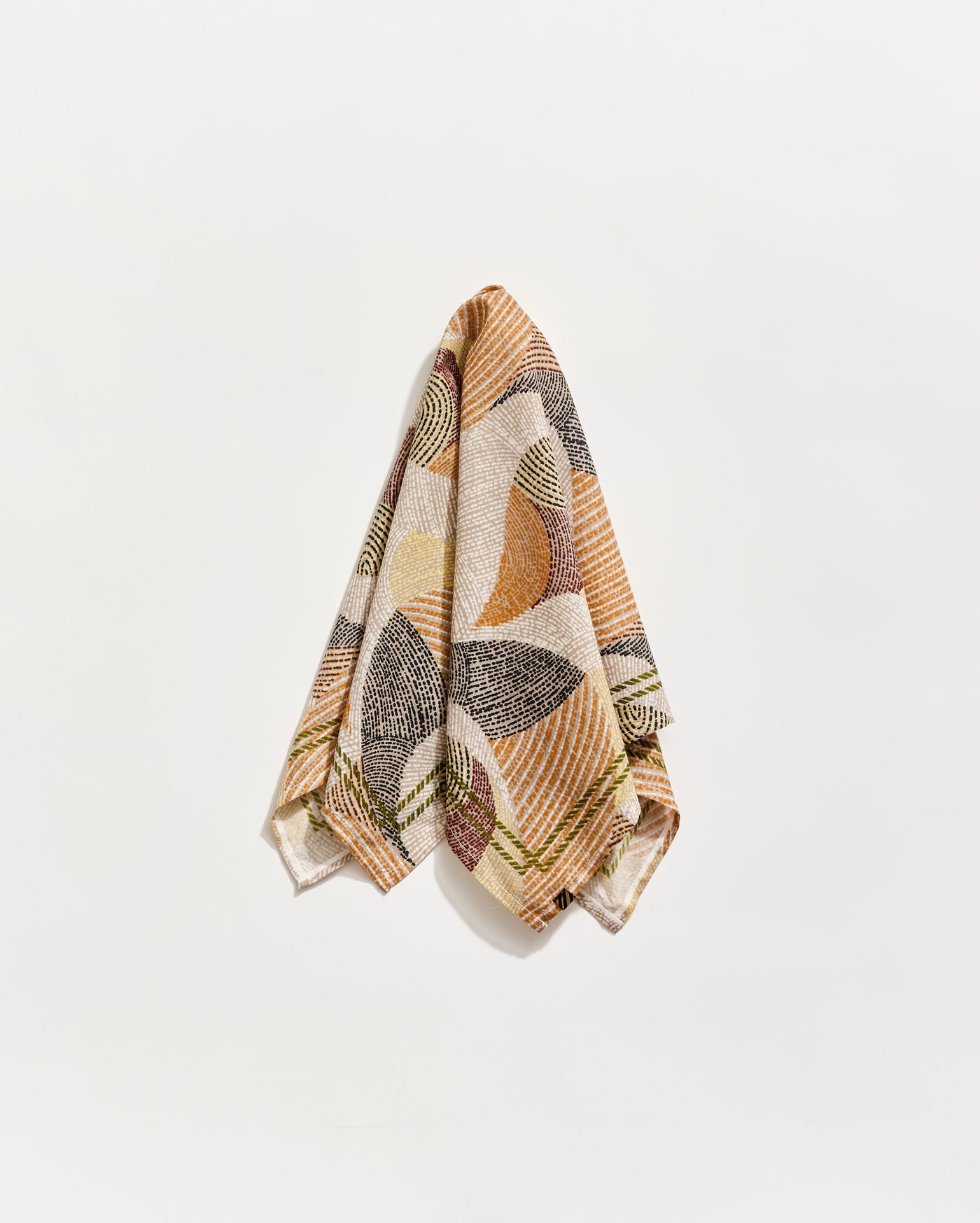 A patterned towel with abstract, geometric designs in earthy tones of brown, orange, green, and cream hangs against a plain white background.
