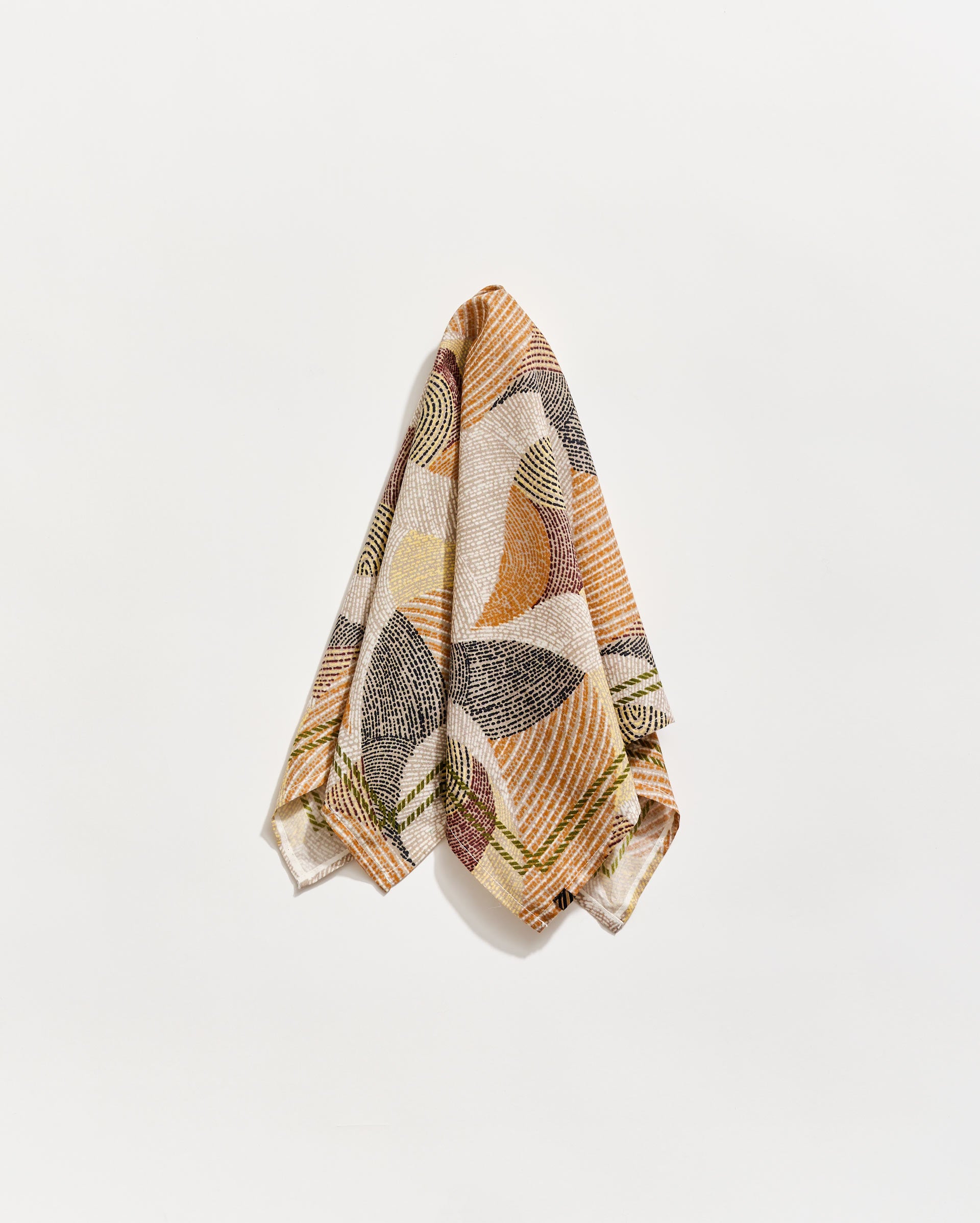 A patterned towel with abstract, geometric designs in earthy tones of brown, orange, green, and cream hangs against a plain white background.