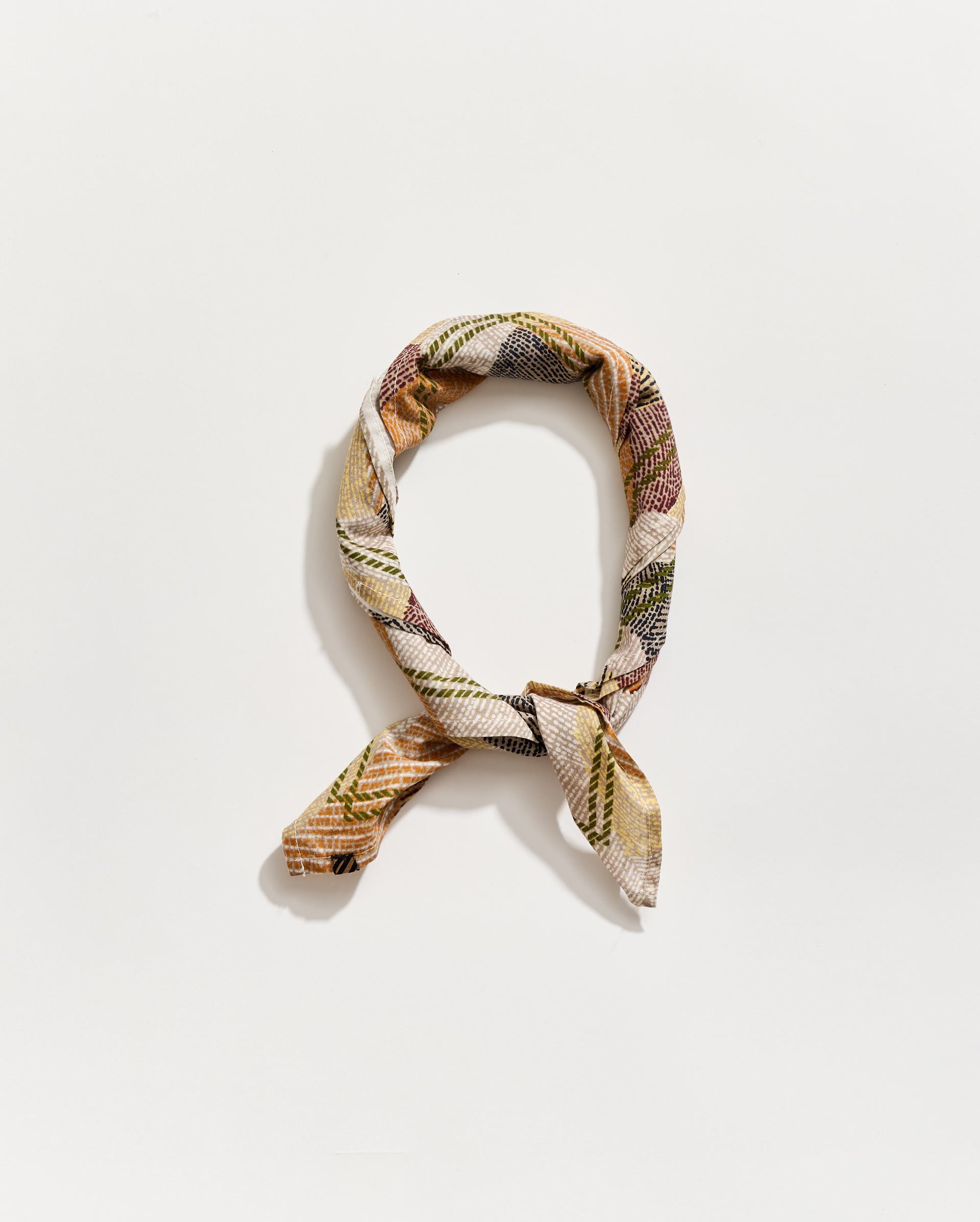 A patterned fabric scarf in muted earth tones arranged in the shape of the letter “Q” on a plain white background.