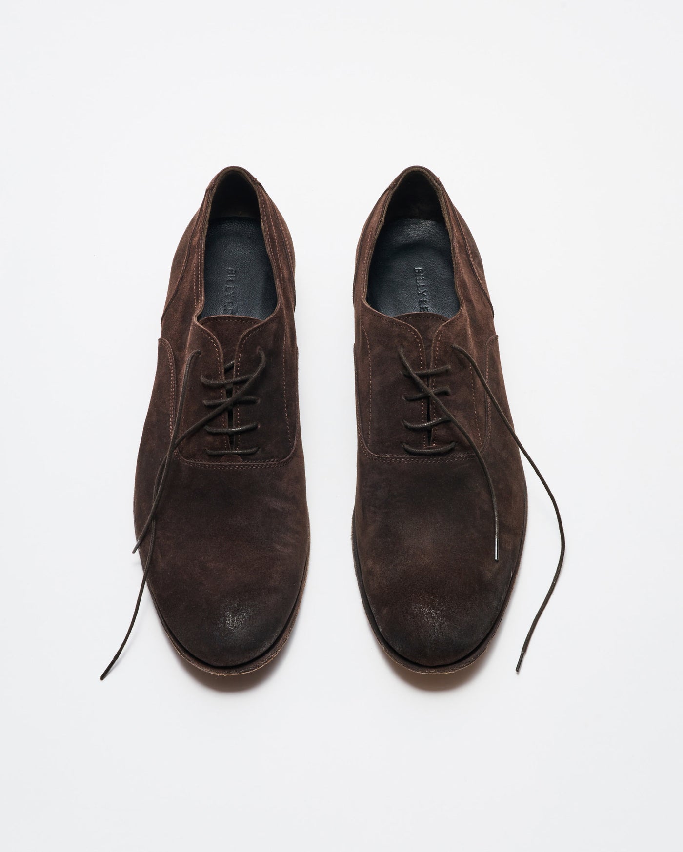 A pair of brown suede lace-up dress shoes is displayed on a white background, with the left shoe fully laced and the right shoes laces partially undone.