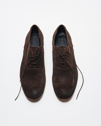 A pair of brown suede lace-up dress shoes is displayed on a white background, with the left shoe fully laced and the right shoes laces partially undone.