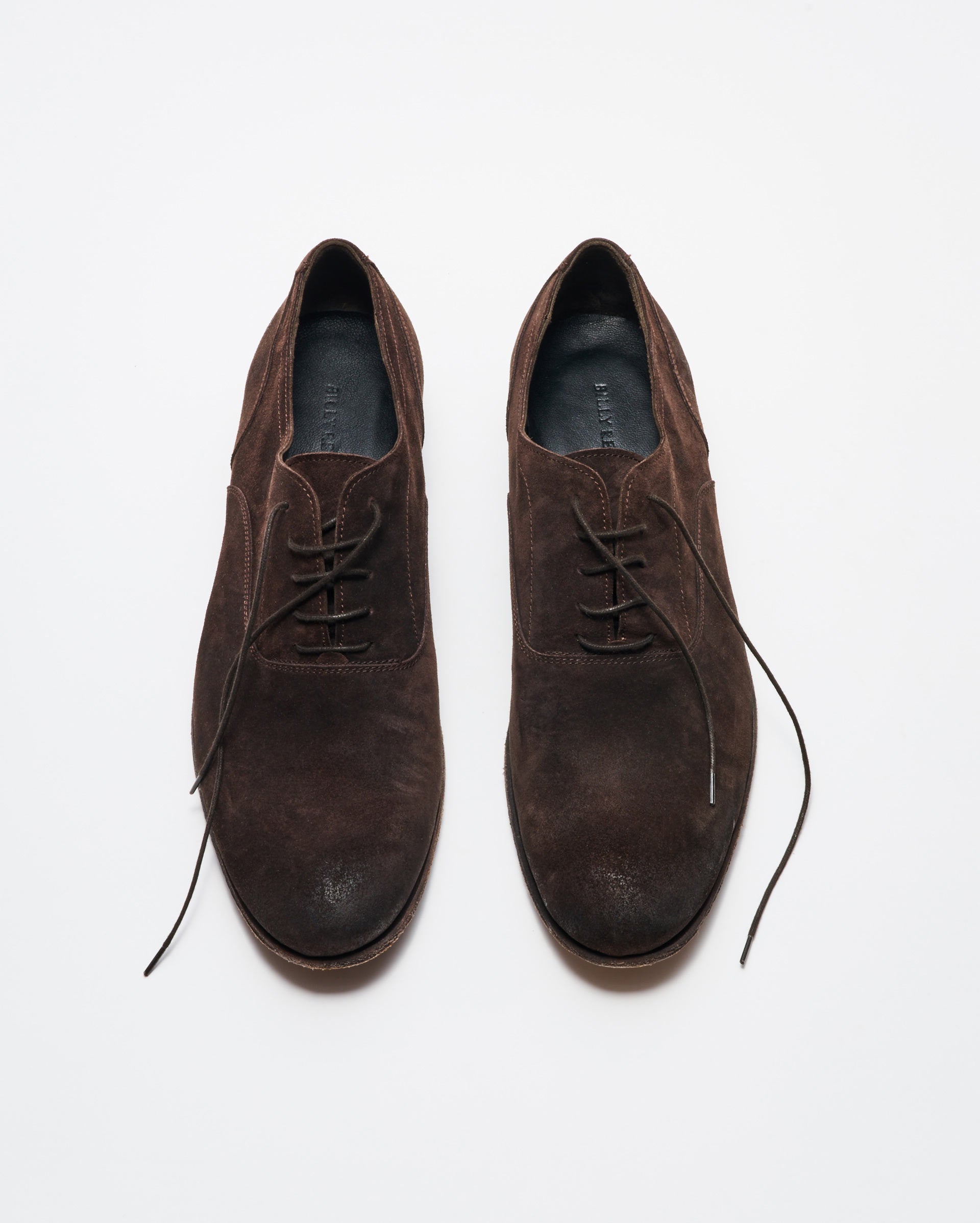 A pair of brown suede lace-up dress shoes is displayed on a white background, with the left shoe fully laced and the right shoes laces partially undone.