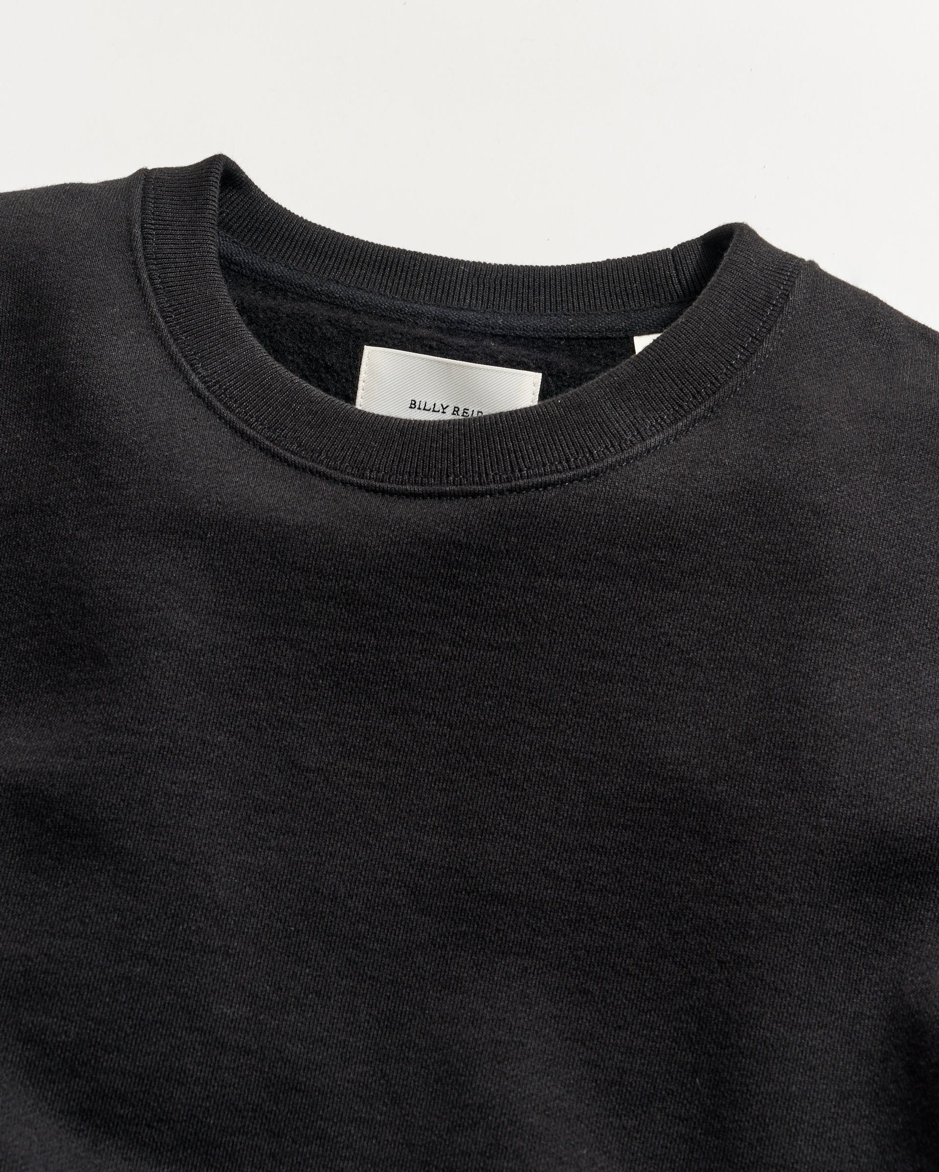 Close-up of a black sweatshirt with a brand label on a light gray background