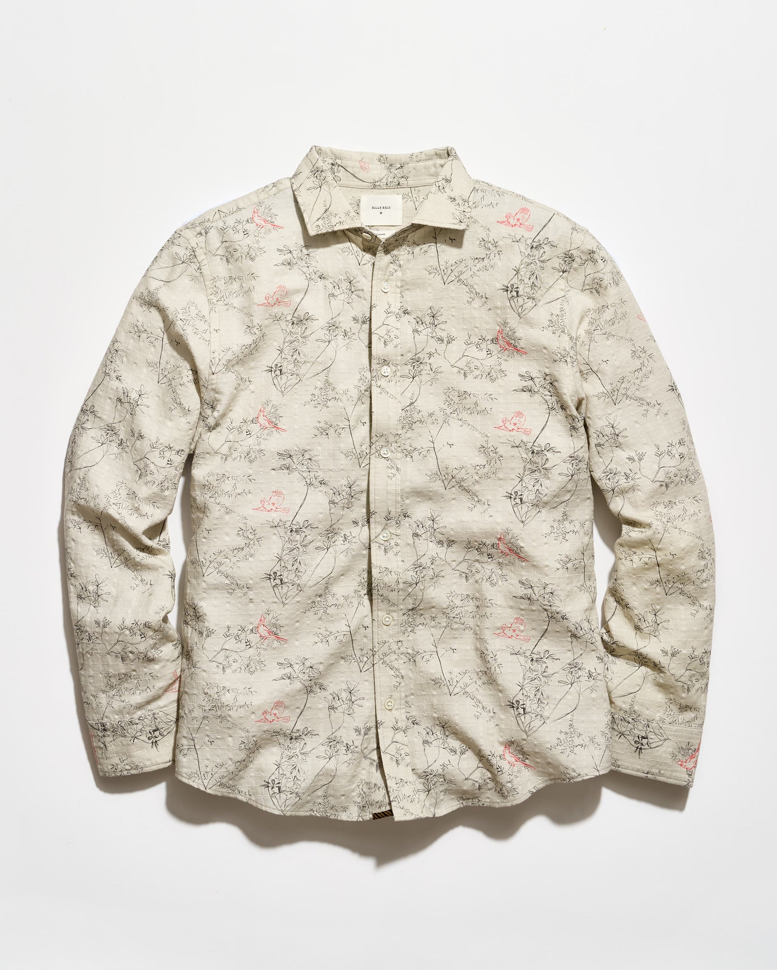 A long-sleeve button-up shirt with a beige base and an all-over delicate floral and branch print in muted pink and gray-green, laid flat against a light background.