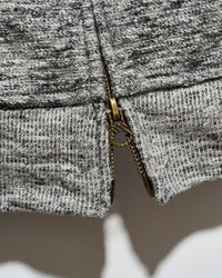 Close-up of a gray and black heathered knit fabric with a gold-tone metal zipper running vertically down the center.
