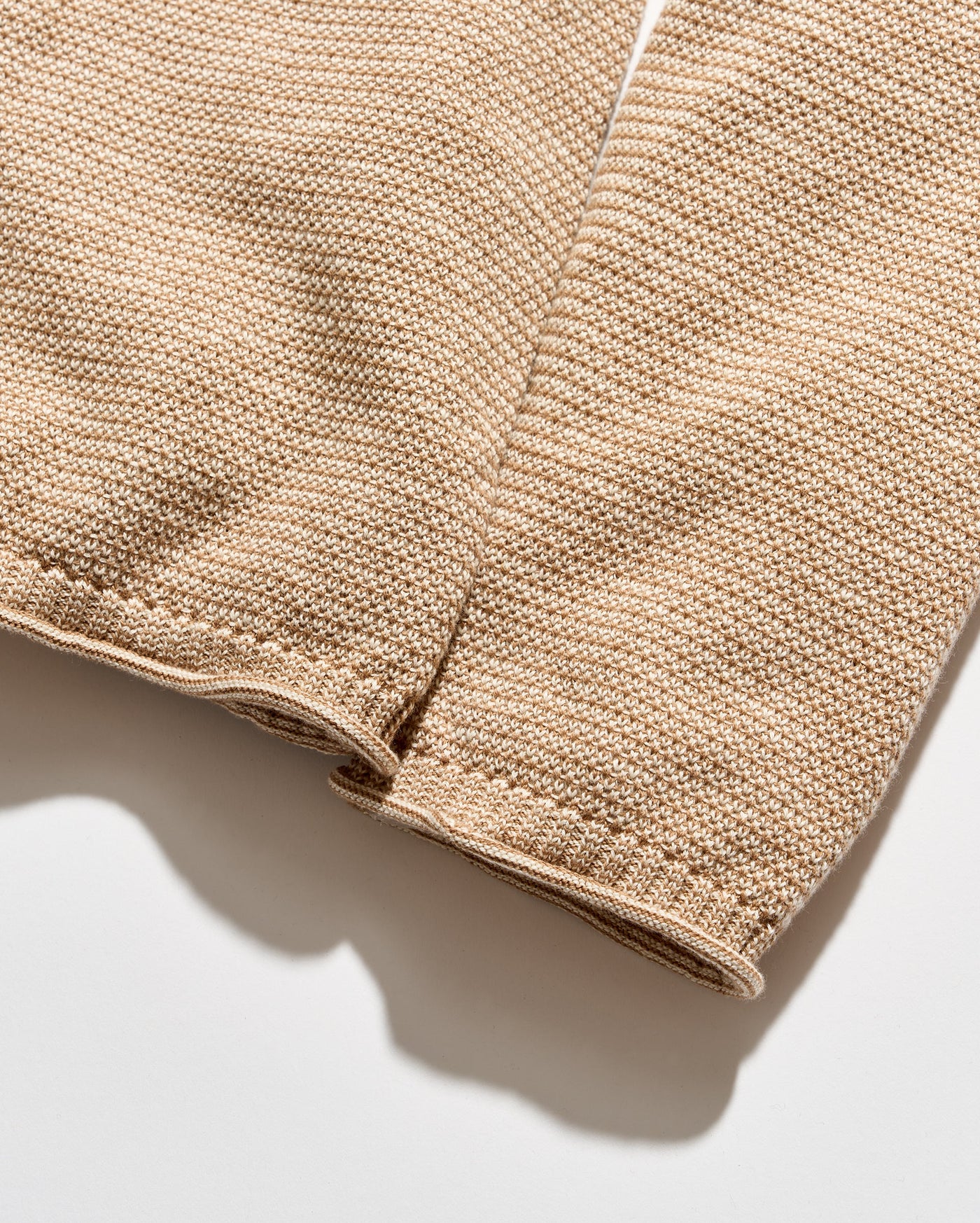 Close-up of a beige knit fabric sleeve or garment detail with visible stitching and a ribbed cuff, photographed on a light neutral background.