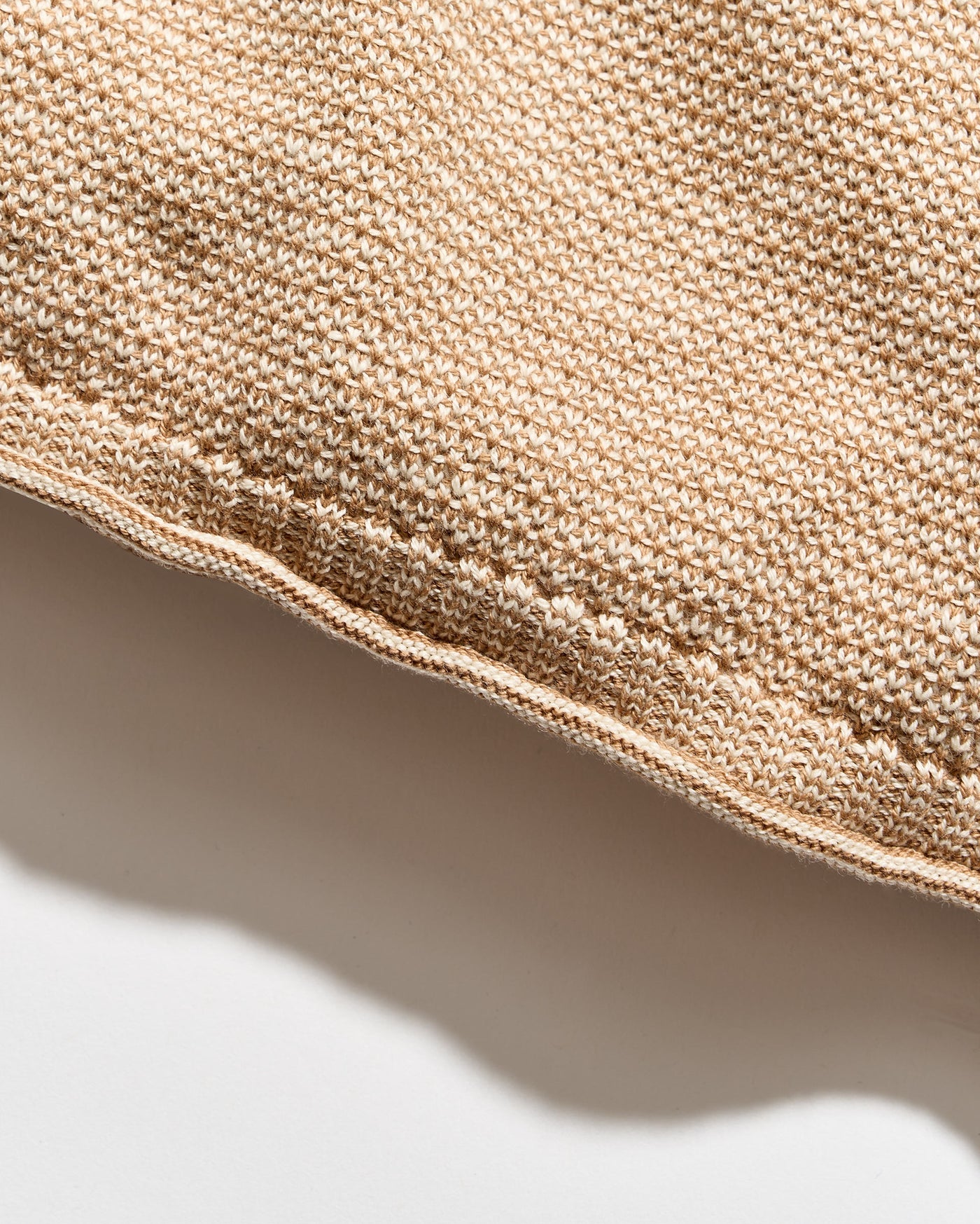 Close-up of a woven textile in a warm beige or tan color, showing the texture and edge of the material against a white background.