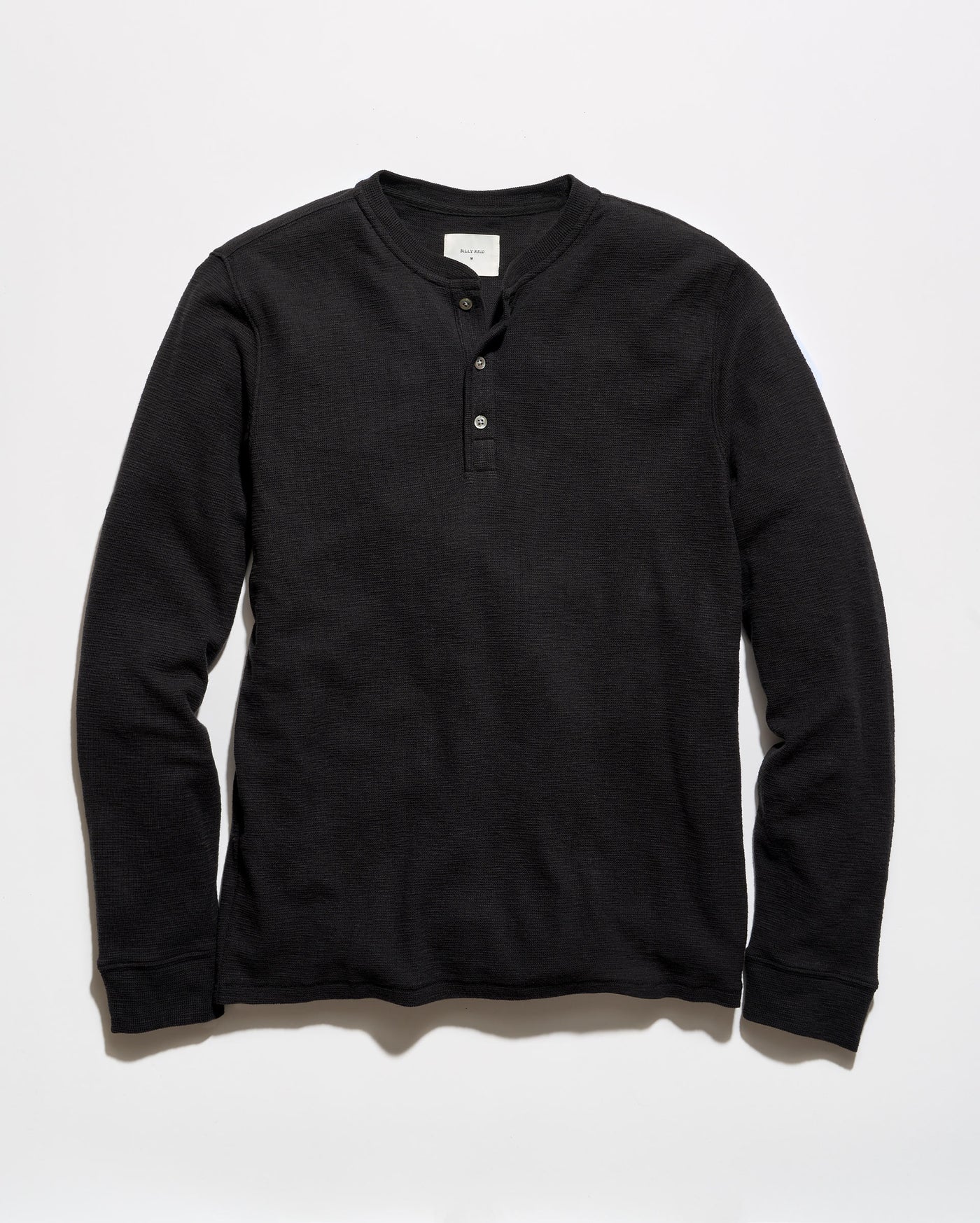 A black long-sleeve henley shirt with a three-button placket, laid flat against a light gray background.